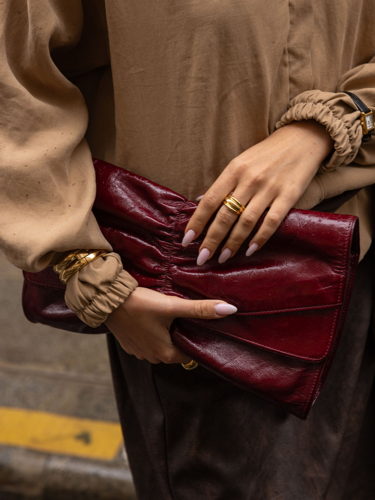 Hands holding a burgundy clutch, wearing gold rings and bracelets